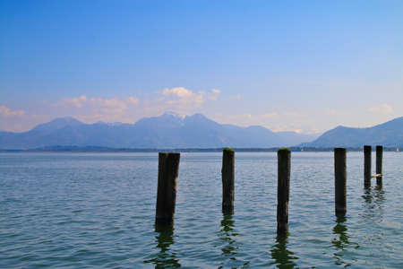 The picture was taken in Germany on Lake Chiemsee. The picture shows a lake visible wooden pillars of the old pier. In the background, the beautiful snow-capped mountains.の写真素材