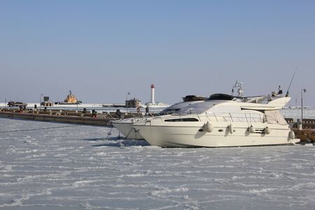 The photo is made in the winter, in the Odessa port. Boats on the winter parking, frozen in ice. The beacon is in the distance visible. Around ice.の写真素材
