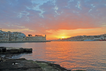 The photo was taken on the island of Malta in the month of January. The picture shows the sunset over the fortification of the city of Singlea. The sun's rays are reflected in the bay of the island.の写真素材