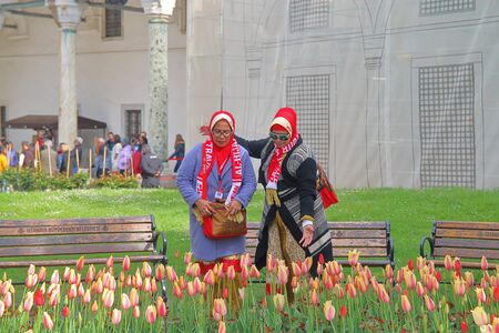 ISTANBUL, TURKEY - APRIL 20, 2019. The photo was taken in the park of Istanbul. The picture shows two middle-aged tourists in bright clothes admiring a flower bed full of tulips.のeditorial素材