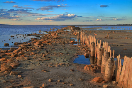 The photo was taken in Ukraine near the estuary called Kuyalnik. The picture shows the remains of a wooden pier on a drying salty estuary in the rays of the setting sun.の写真素材