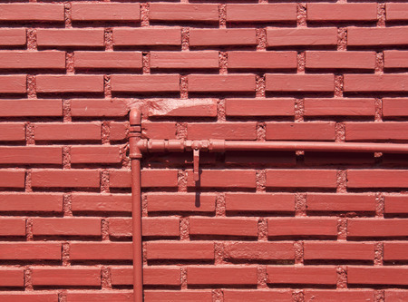 Red brick wall with water pipes and shut-off valve open.の写真素材