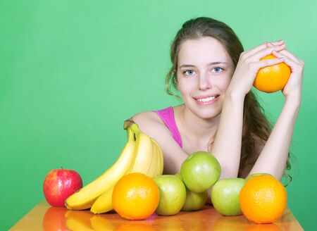 Portrait of young beautiful woman with fruits on a green backgroundの写真素材