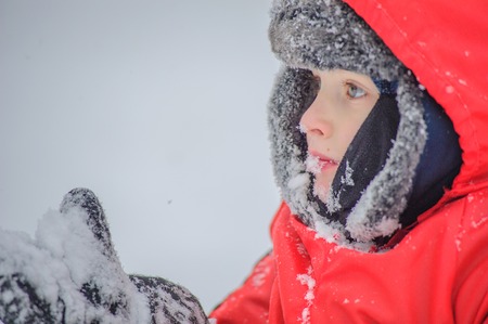 A blue eyed 8 years old boy licking his mitten and eating snow, close up portraitの写真素材