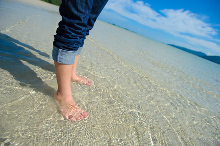 Close up of child's feet walking on crystal clear tropical sea water