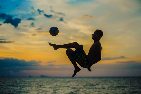 Kicking a ball. Silhouette of a man on a beach. Sunset behindの写真素材