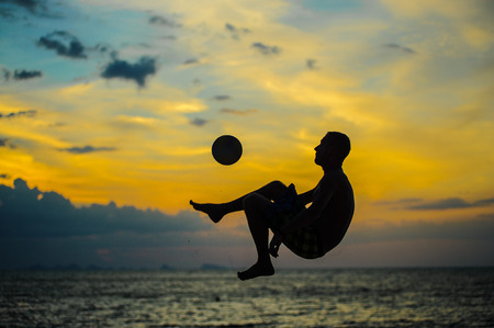 Kicking a ball. Silhouette of a man on a beach. Sunset behindの写真素材