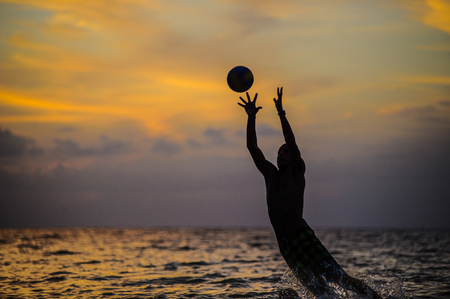 Catching a ball. Silhouette of a man jumping out of sea water.の写真素材