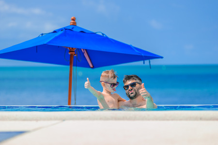 Seven years old cute boy smiling without tooth. He and his bearded father are in sunglasses, show...
