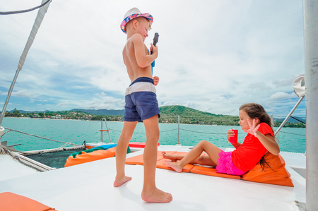 Cute kids on a boat trip. Boy is playing a toy guitar for his beautiful girlfriendの写真素材
