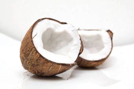 Closeup of cracked coconut on white background with light shadow. Shallow focus depth on front coconut の写真素材