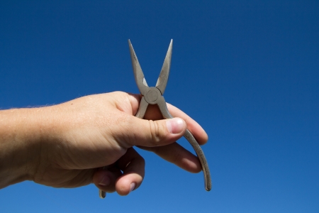 Pliers in hand man on a background of blue skyの写真素材
