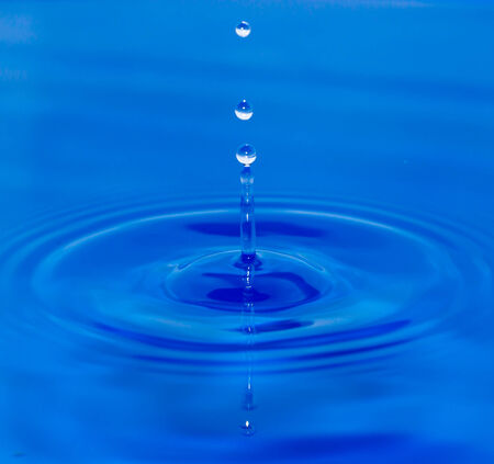A drop of water falling in blue waterの写真素材