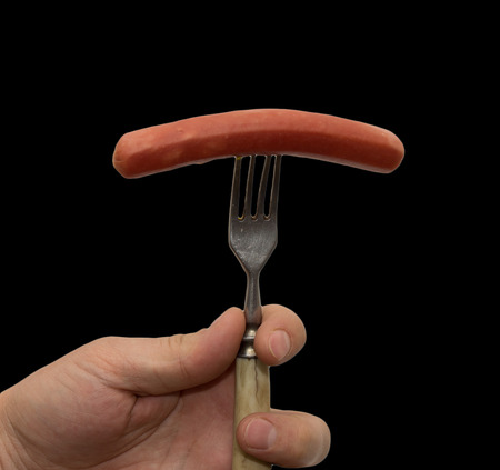 sausage on a fork in his hand on a black backgroundの写真素材