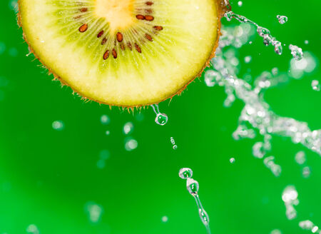 kiwi fruit in a spray of water on a green backgroundの写真素材