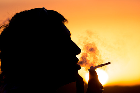 Silhouette of male smokers in the sunsetの写真素材