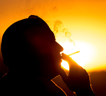 Silhouette of male smokers in the sunsetの写真素材