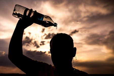 man pours water on his head in the sunsetの写真素材