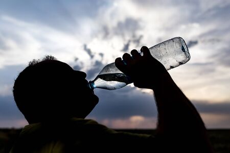 silhouette of a man drinking water at sunsetの写真素材