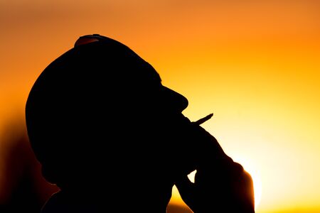 Silhouette of male smokers in the sunsetの写真素材