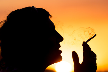 Silhouette of male smokers in the sunsetの写真素材