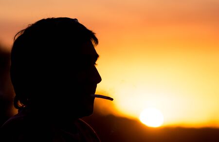 Silhouette of male smokers in the sunsetの写真素材