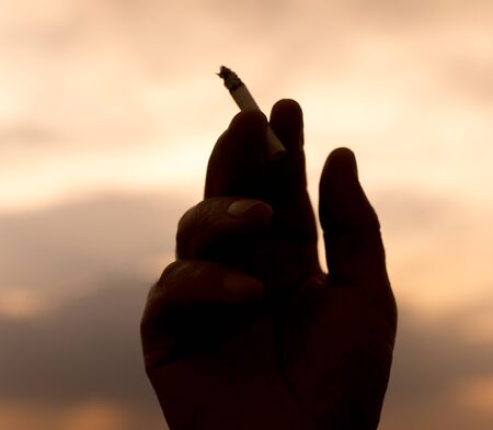 silhouette hand with a cigarette on a sunset backgroundの写真素材