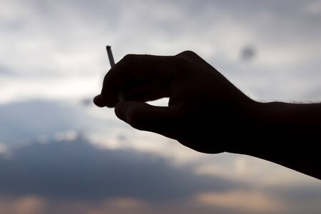 silhouette hand with a cigarette on a sunset backgroundの写真素材