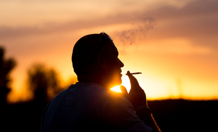 Silhouette of male smokers in the sunsetの写真素材