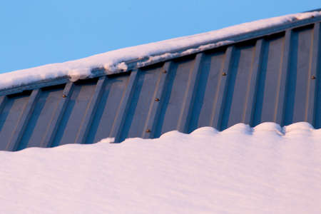 Snow on the roof of the house at sunset .の写真素材