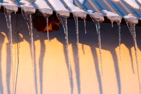 Icicles on the roof of the house at sunset .の写真素材