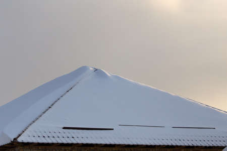 Snow on the roof of the house at sunset .