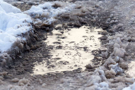 Snow with puddles on the road at sunset as backgroundの写真素材