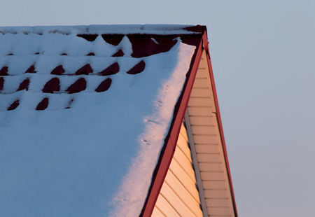 Snow on the roof of the house at sunset .の写真素材