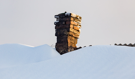 Snow on the roof of the house at sunset .の写真素材