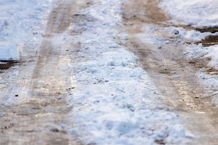 Snow with puddles on the road at sunset as backgroundの写真素材
