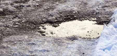 Snow with puddles on the road at sunset as backgroundの写真素材