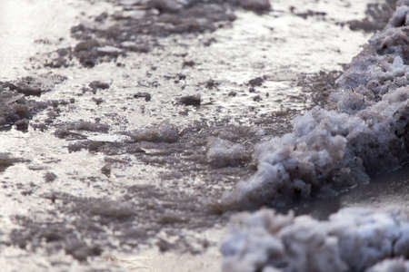 Snow with puddles on the road at sunset as backgroundの写真素材