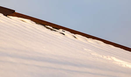 Snow on the roof of the house at sunset .の写真素材