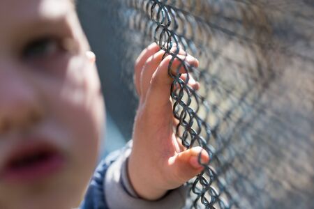 The boy stands near the metal fence .の写真素材