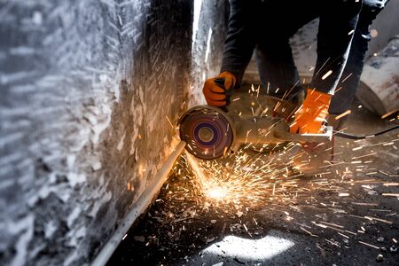 Worker cuts a metal pipe with sparks .