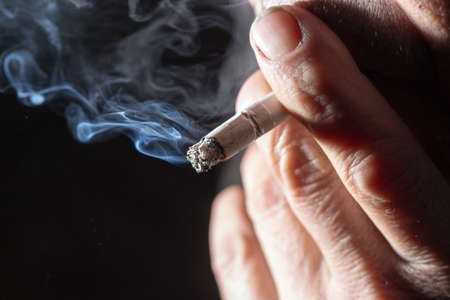 Cigarette smokes in hand on a black backgroundの写真素材