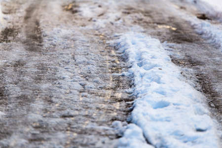 Snow with puddles on the road at sunset as backgroundの写真素材