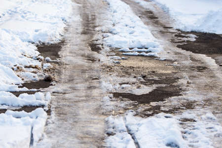 Snow with puddles on the road at sunset as backgroundの写真素材