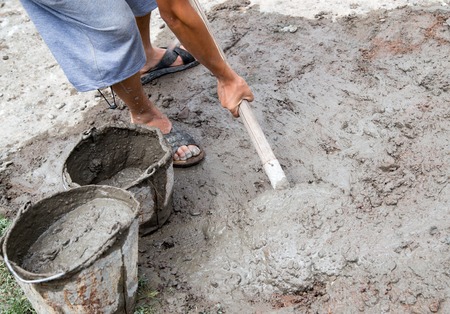 Worker mixes concrete with a shovel at the construction site