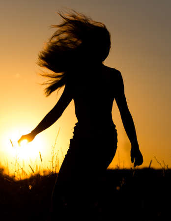 Silhouette of a girl with long hair at sunset .の写真素材
