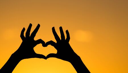Silhouette of the heart by hands at sunset .の写真素材