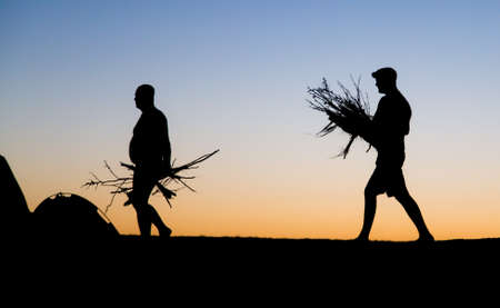 Silhouette of a man with firewood at sunsetの写真素材