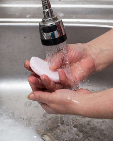 Woman washes her hands with soap under a tap of waterの写真素材