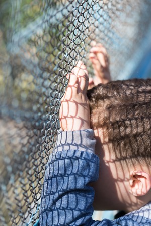 The boy stands near the metal fenceの写真素材